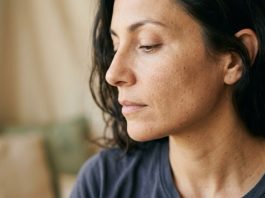 Primo piano del viso di una donna su sfondo neutro beige, luce naturale morbida, pelle senza trucco.