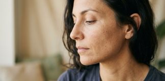 Primo piano del viso di una donna su sfondo neutro beige, luce naturale morbida, pelle senza trucco.